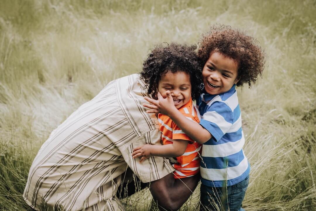 Man hugging his two young boys in a grass field