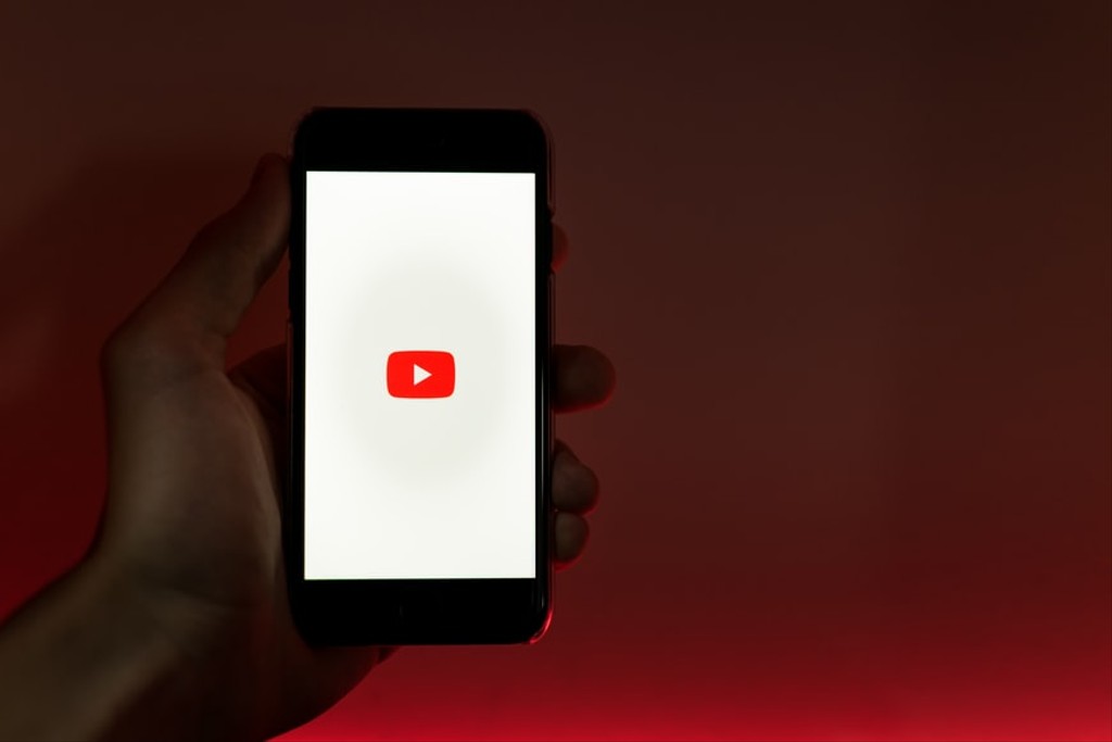 Person holding a smartphone with the YouTube logo showing on a white screen