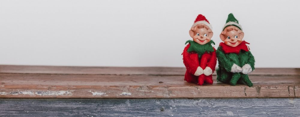Two Christmas elf decorations in a sitting position on a wood ledge
