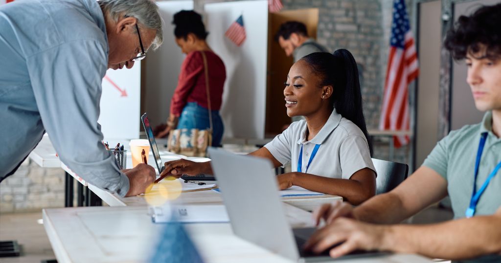 Young woman working at election table helping older man sign in