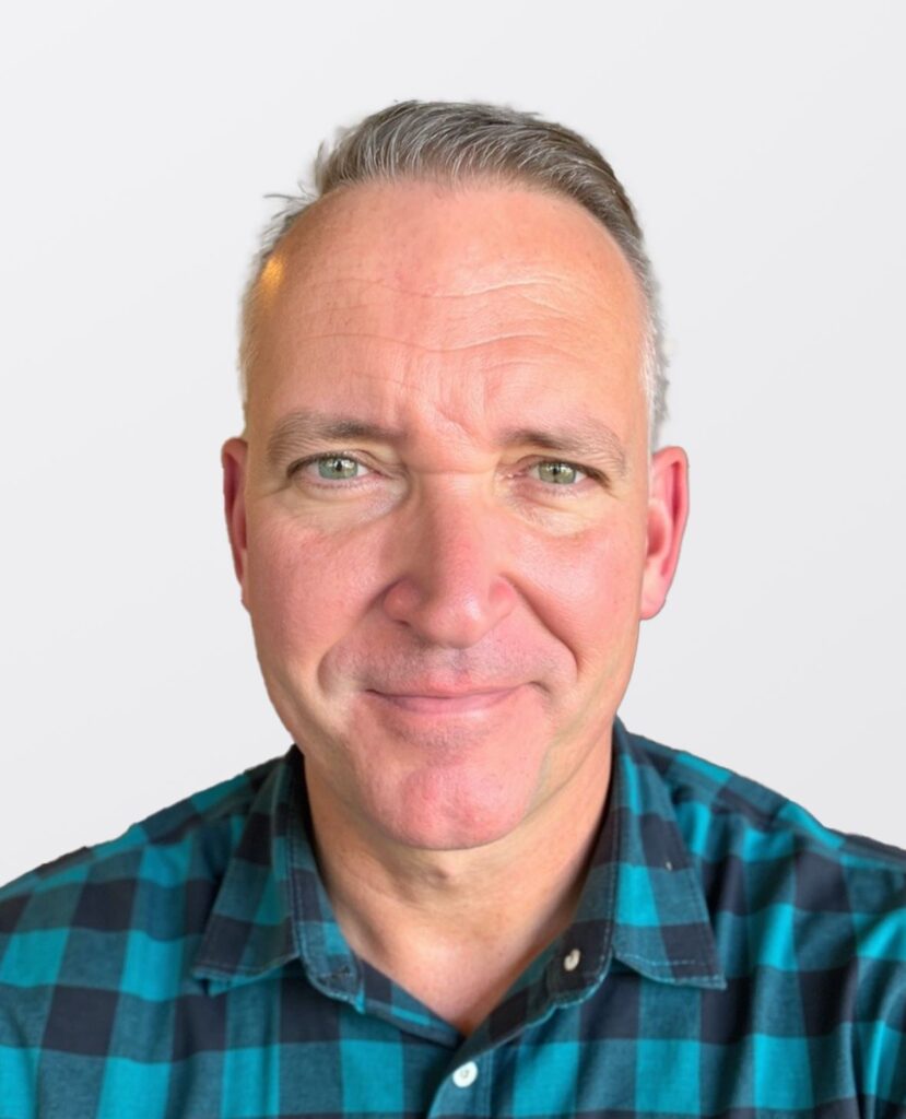 Professional headshot of a smiling man in a plad shirt.